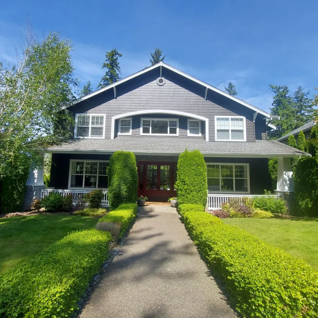A two-story dark gray house with a red front door, white trim, and trimmed bushes lining the walkway.