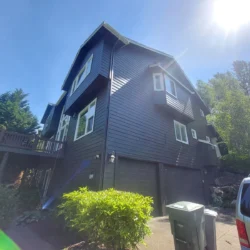 A dark blue two-story house with white trim, a double garage, and trash bins on a sunny day.