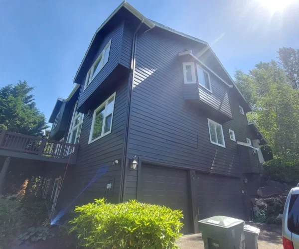 A dark blue two-story house with white trim, a double garage, and trash bins on a sunny day.