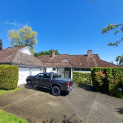 A black pickup truck is parked in the driveway of a suburban house with a brown roof and white garage doors.