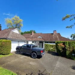 A black pickup truck is parked in the driveway of a suburban house with a brown roof and white garage doors.