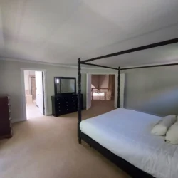 Spacious bedroom with a four-poster bed, dresser with mirror, and view into a bathroom and hallway.