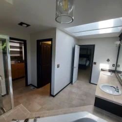 Bathroom with beige tile floor, double sinks, a bathtub, glass shower, and two doorways leading to other rooms.