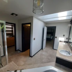 Bathroom with beige tile floor, double sinks, a bathtub, glass shower, and two doorways leading to other rooms.