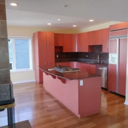 Modern kitchen with reddish-pink cabinets, stainless steel appliances, granite countertops, and hardwood floors.