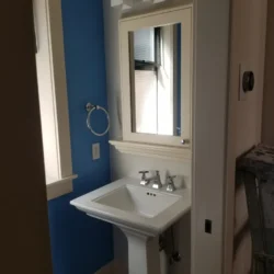 A white pedestal sink with a mirror above it in a small bathroom with blue and white walls.