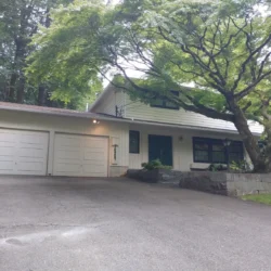 Two-car garage and driveway in front of a two-story house with large trees and stone landscaping.