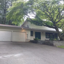 Two-car garage and driveway in front of a two-story house with large trees and stone landscaping.