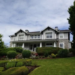 Two-story white house with covered porch, stone accents, and neatly landscaped front yard under a partly cloudy sky.