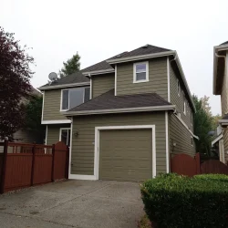 Two-story suburban house with green siding, attached garage, and brown fence on a cloudy day.