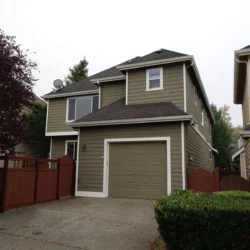 Two-story suburban house with green siding, attached garage, and brown fence on a cloudy day.