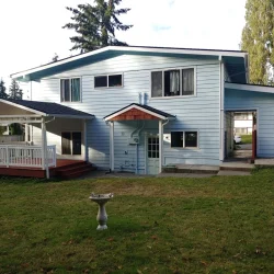 Two-story blue house with a covered porch, concrete patio, and grassy backyard with a birdbath.